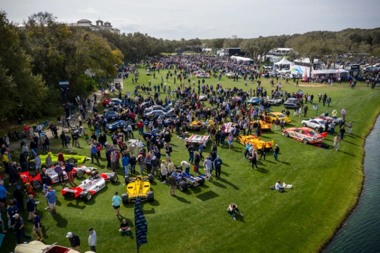 Racing cars ranked across the fairway with the crowd walking between them, seen from above at the Amelia Island Concours d’Elegance, an engagement in the season calendar of The Mansa Court