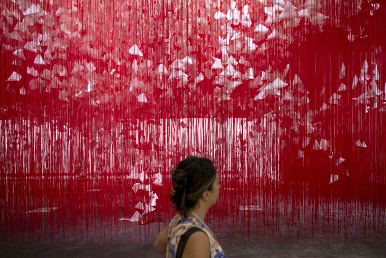 A visitor passing a room-filling installation of red thread and white paper at Art Basel, a mid-June engagement in the season calendar of The Mansa Court