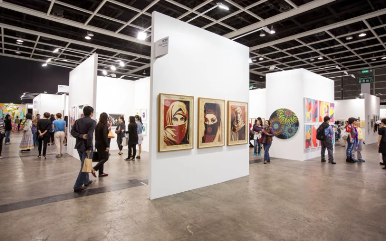 Visitors between white gallery stands hung with framed prints at Art Basel Hong Kong, the March fair at the Convention and Exhibition Centre in the season calendar of The Mansa Court