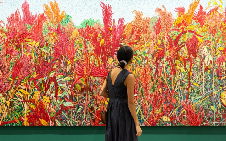 A visitor standing before a large red and green painting at Art Basel Hong Kong, the Asian art fair in the season calendar of The Mansa Court
