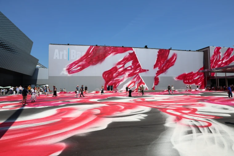 Visitors crossing the Messeplatz, its ground and the hall façade painted in sweeping red and white, beside Messe Basel during Art Basel, a mid-June engagement in the season calendar of The Mansa Court