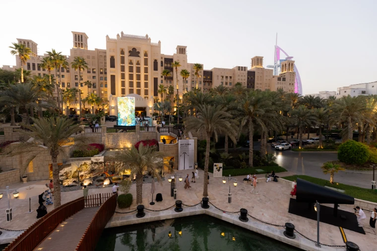 Madinat Jumeirah at dusk during Art Dubai, a digital artwork glowing before the wind-towered hotel and the Burj Al Arab beyond, an early-April engagement in the season calendar of The Mansa Court