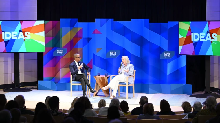 Two speakers in conversation on the main stage before a bright geometric set and an attentive audience at the Aspen Ideas Festival, a late-June engagement in the season calendar of The Mansa Court