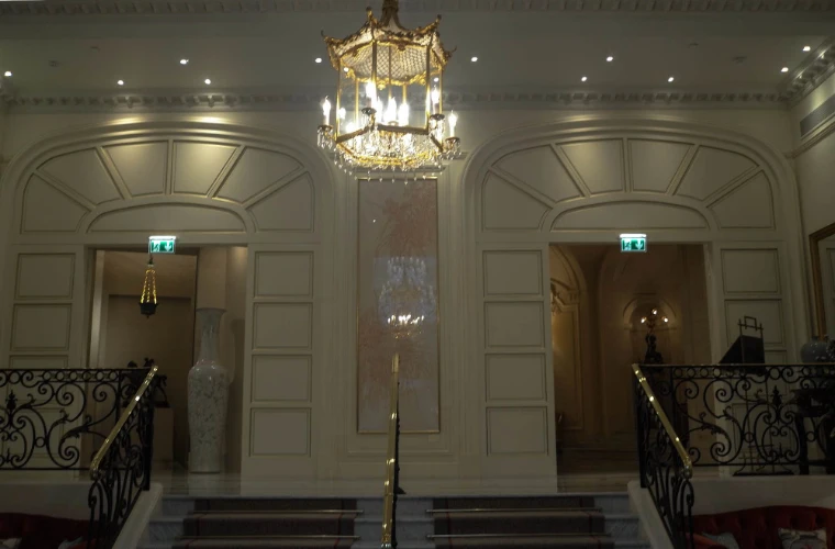 A pale panelled stair hall in the Shangri-La Paris, with a gilt chandelier hanging between twin doorways and wrought-iron stair rails (2012).