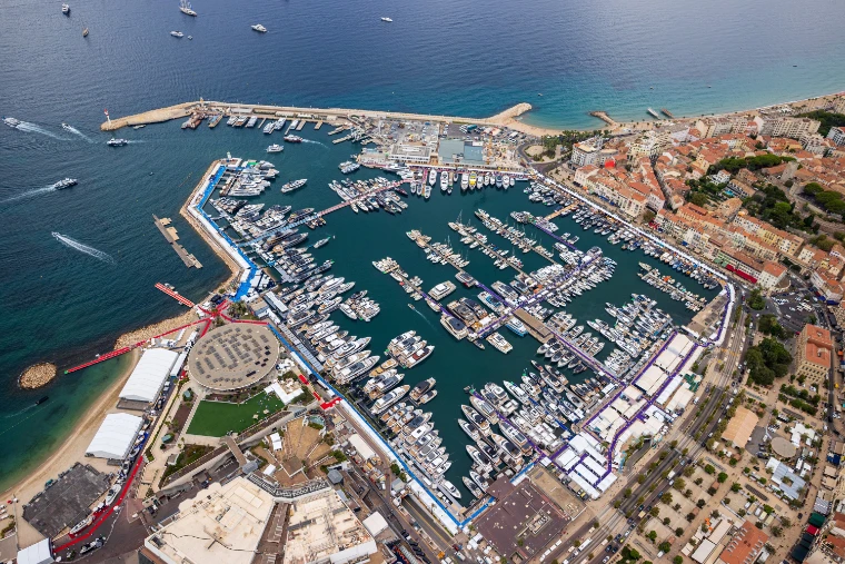 An aerial view of the Palais des Festivals and its round pavilion beside the Vieux Port, the basin filled with yachts on show and the harbour wall curving out to sea (2026).