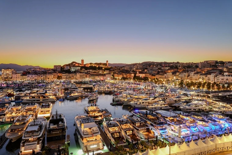 The Vieux Port at dusk, its moored yachts lit along the pontoons and the lit town hall and old town behind under a fading orange sky (2026).