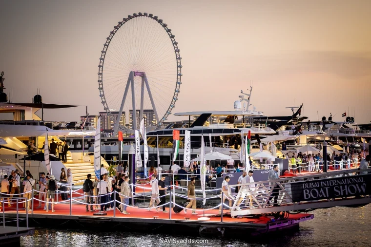 Superyachts and a classic wooden motor yacht berthed along the red pontoons with Ain Dubai beyond at the Dubai International Boat Show, an engagement in the season calendar of The Mansa Court