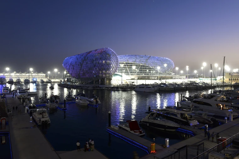 The hotel’s lit lattice shell glows purple and blue at dusk above the marina, with motor yachts moored at the pontoons in the foreground (2013).