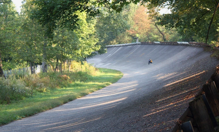 A curve of the old concrete banked oval at Monza rises among green trees in low morning sun (2010).