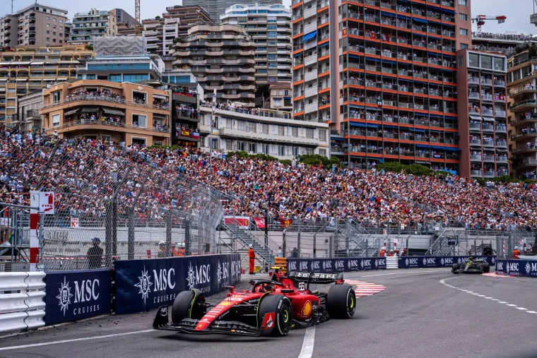 A car rounds the swimming pool section before packed grandstands and flag-hung balconies. The Formula 1 Monaco Grand Prix on the streets of Monte Carlo, in the season calendar of The Mansa Court