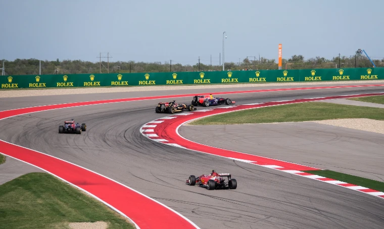 Four Formula One cars threading through the red-and-white kerbed S-bends beside a line of Rolex boards (2014).