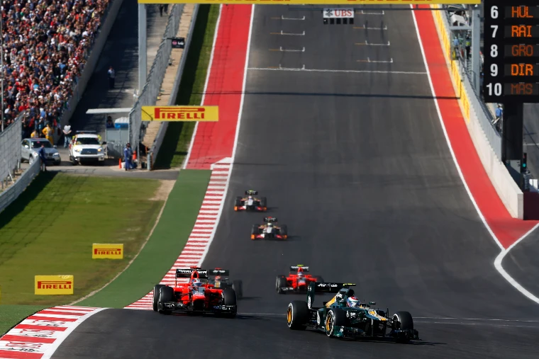 Formula One cars in a line climbing the steep hill towards Turn 1 at the end of the first lap, with spectators along the bank (2012).
