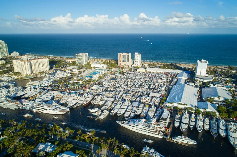 An aerial view of a marina packed with hundreds of white yachts and show tents, with hotels, the beach and the Atlantic beyond (2017).
