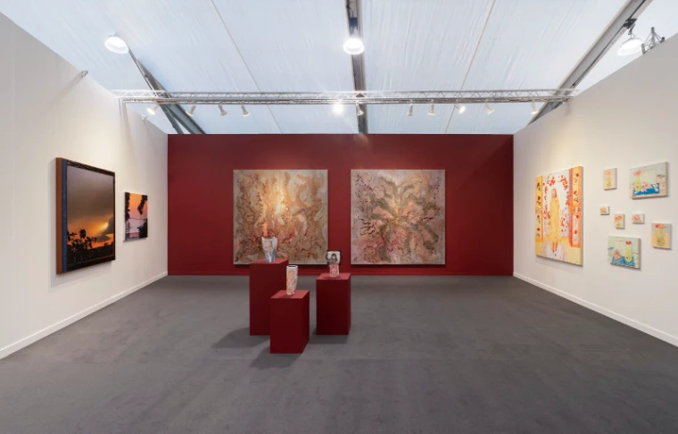 Large paintings on a deep red wall with ceramics on plinths in a gallery booth at Frieze Los Angeles, an engagement in the season calendar of The Mansa Court