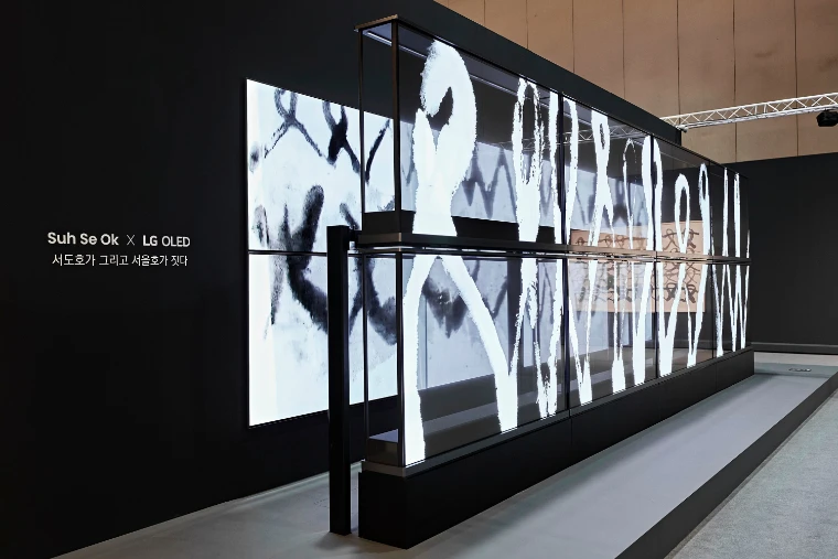 Black and white ink brushwork glows across a long row of transparent screens in a darkened exhibition space (2024).