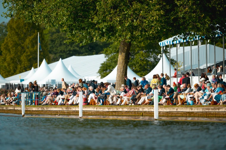 Spectators crowd the bank of the Regatta Enclosure beneath a tree and the white marquees.