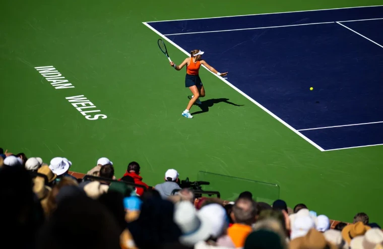 A player striking a forehand on the stadium court with INDIAN WELLS painted on the green at the BNP Paribas Open, Indian Wells, California, a March engagement in the season calendar of The Mansa Court