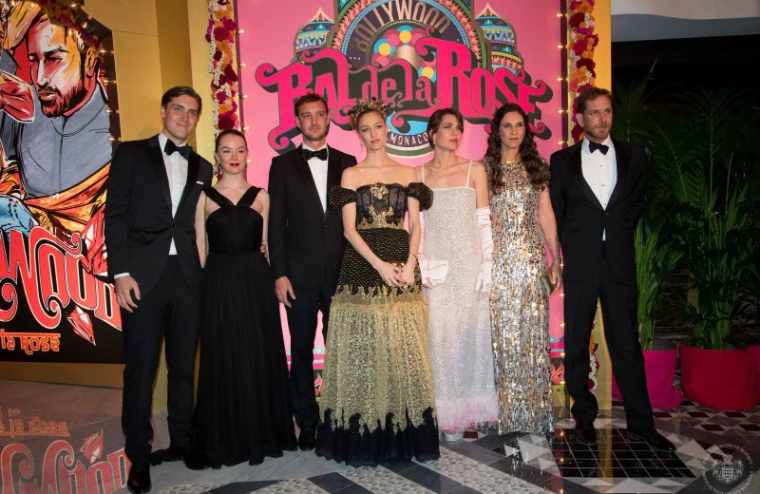 Guests in black tie and evening gowns photographed before the themed Bal de la Rose backdrop at Monte Carlo, an engagement by invitation in the season calendar of The Mansa Court