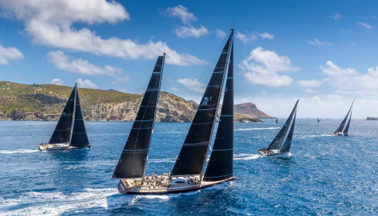 Maxi yachts under black sails racing past the rocky coast at Les Voiles de Saint-Barth, St. Barthélemy, a mid-April engagement in the season calendar of The Mansa Court