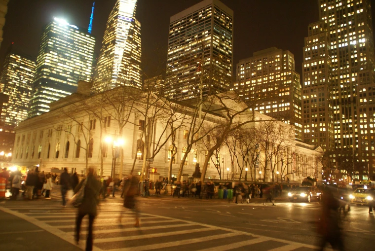 The Library’s marble front glowing in lamplight on a winter night beneath lit Midtown towers, people crossing the street in front (2013).