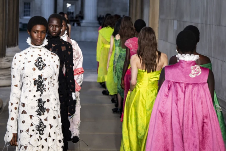 Models in acid green, magenta and cut lace walking a runway through a stone colonnade at London Fashion Week, an engagement in the season calendar of The Mansa Court