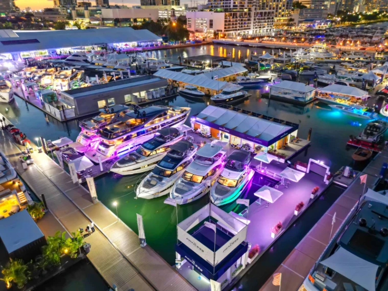 An aerial view of the show marina at dusk with motor yachts berthed in ranks under coloured light at the Miami International Boat Show, Miami Beach, an engagement in the season calendar of The Mansa Court