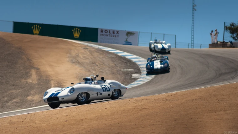 Three vintage sports racing cars descend the steep twisting Corkscrew at Laguna Seca, with Rolex boards and spectators on the hill above (2014).