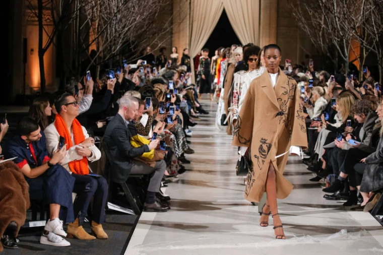 An embroidered camel coat on the runway as the front row raises its phones at New York Fashion Week, an engagement in the season calendar of The Mansa Court