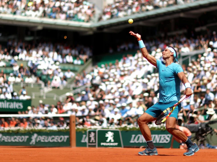 A left-handed serve tossed high above the clay before a full Court Philippe-Chatrier. The Roland Garros finals on Court Philippe-Chatrier, Paris, in the season calendar of The Mansa Court