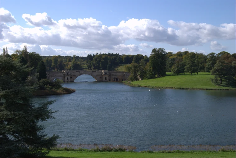 Vanbrugh’s Grand Bridge seen across the Great Lake, framed by dark conifers and green parkland under a broken summer sky (2008).