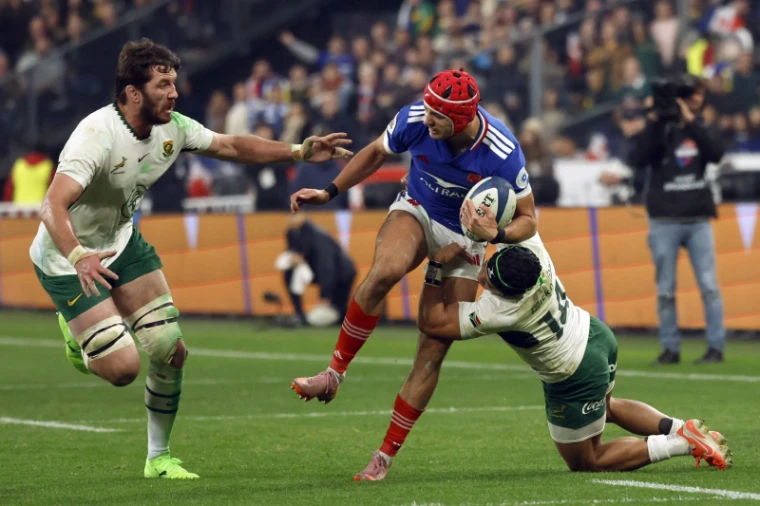 A winger in a red scrum cap carrying the ball into contact and breaking a tackle near the line under floodlight, at Six Nations Championship, an engagement in the season calendar of The Mansa Court