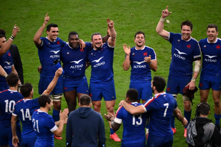 Players in blue arm in arm on the pitch with arms raised to the stands after a Six Nations Championship victory, an engagement in the season calendar of The Mansa Court