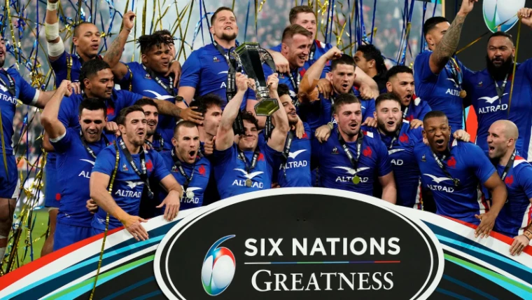 The France squad in blue lifting the Six Nations Championship trophy under gold and blue streamers on the presentation stage, an engagement in the season calendar of The Mansa Court