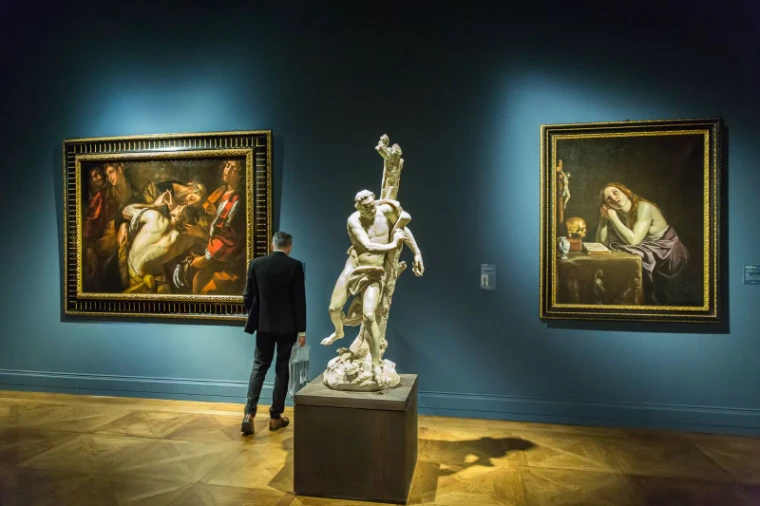 A visitor studying old master paintings and a marble sculpture on a blue-walled stand at TEFAF Maastricht, an engagement in the season calendar of The Mansa Court