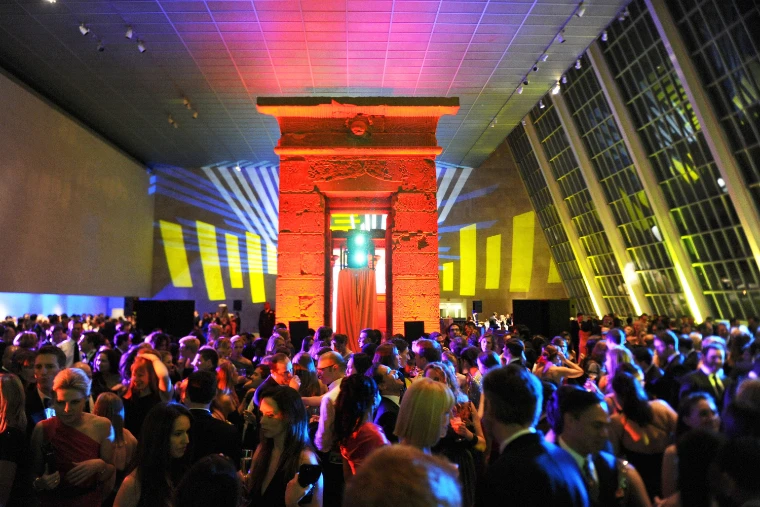 Guests in black tie crowd the dance floor before the Temple of Dendur, lit red, under coloured lights in the Sackler Wing (2011).
