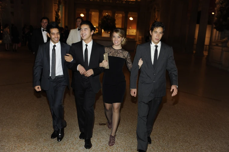 Four guests in dark suits and a black cocktail dress walk arm in arm through the Great Hall of the Met at night (2010).