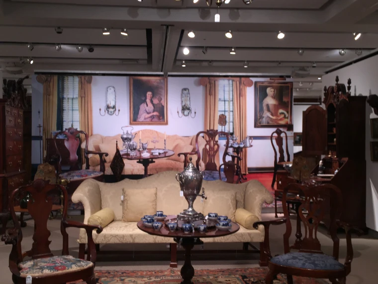 A pre-sale exhibition gallery at Sotheby's set out as a period drawing room, with a yellow silk sofa, mahogany chairs, a silver urn on a tea table and two eighteenth-century portraits on the wall (2016). Sotheby's, Upper East Side, New York, shown for The Auction House Previews in the season calendar of The Mansa Court