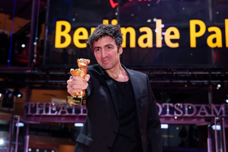 A winning director holding the Golden Bear out to the cameras outside the lit Berlinale Palast at The Berlinale, an engagement in the season calendar of The Mansa Court