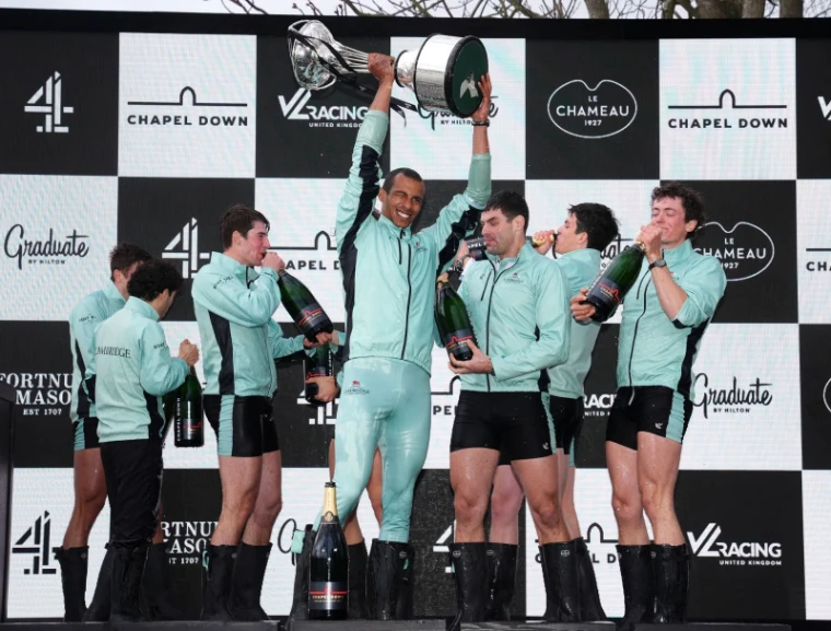 The winning crew lifting the trophy and drinking champagne after The Boat Race on the Tideway, London, an engagement in the season calendar of The Mansa Court
