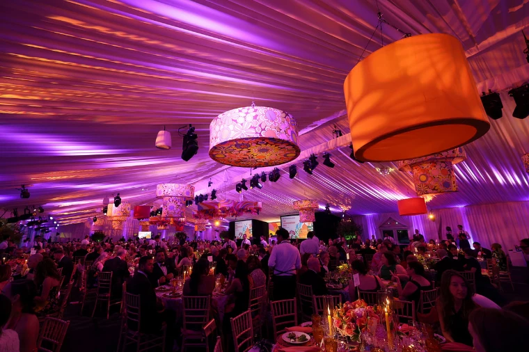 Guests at dinner in the tent, beneath lampshades hung with flowers and lit pink and violet (2026). The Conservatory Ball at the New York Botanical Garden, the Bronx, in the season calendar of The Mansa Court