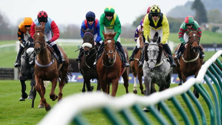 Steeplechasers in bright silks galloping towards the camera past the running rail, National Hunt racing as run at the Grand National, Liverpool, an April engagement in the season calendar of The Mansa Court