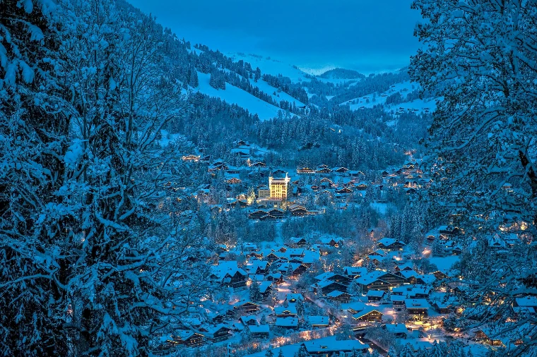 Gstaad at blue hour under fresh snow, the lit tower of the Gstaad Palace standing above the chalets of the village and the snow-laden forest (2011).