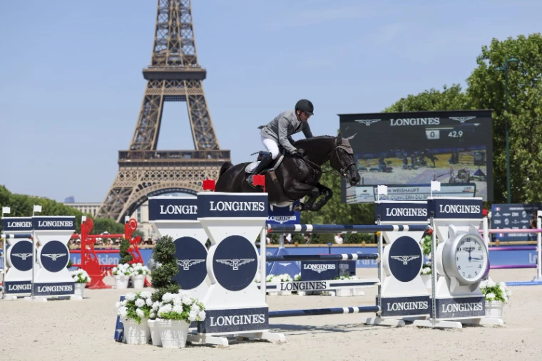 A horse and rider over a Longines fence beside the tour clock with the Eiffel Tower behind at the Longines Global Champions Tour in Paris, an engagement in the season calendar of The Mansa Court