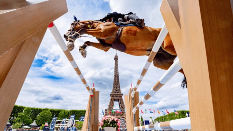 A horse and rider seen from beneath the fence with the Eiffel Tower framed between the standards at the Longines Global Champions Tour, Paris, an engagement in the season calendar of The Mansa Court
