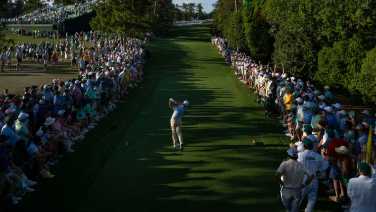 A player driving down a pine-lined fairway between the galleries in late light at The Masters, Augusta National, Georgia, an April engagement in the season calendar of The Mansa Court
