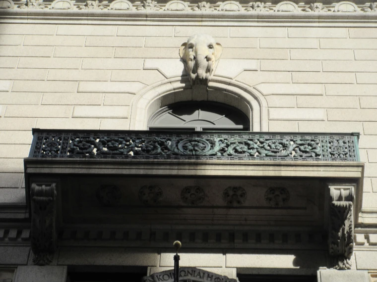 A carved stone elephant’s head above an arched window and an ornate iron balcony on the façade of the University Club (2019).