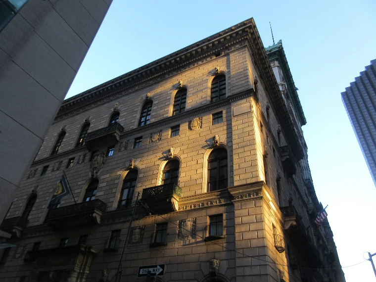 The granite palazzo of the University Club rising above Fifth Avenue, its upper floors lit gold by low winter sun against a pale blue sky (2021).