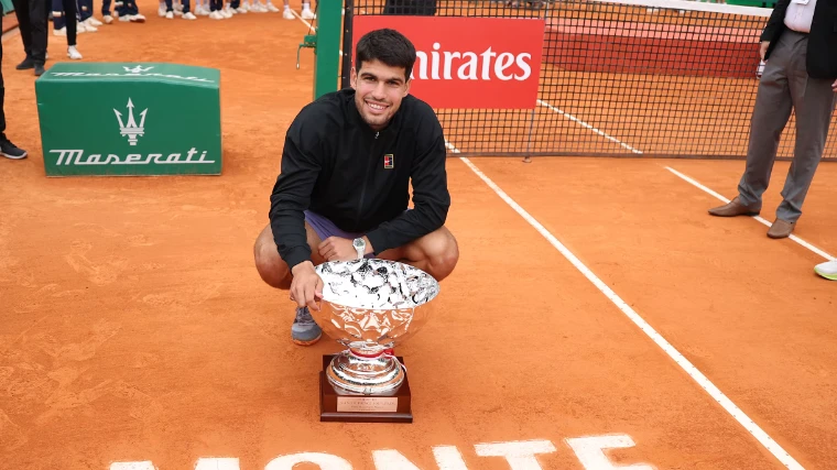 Carlos Alcaraz crouching beside the Coupe de S.A.S. le Prince Souverain on the clay after winning the 2025 Rolex Monte-Carlo Masters, Monte Carlo, an April engagement in the season calendar of The Mansa Court