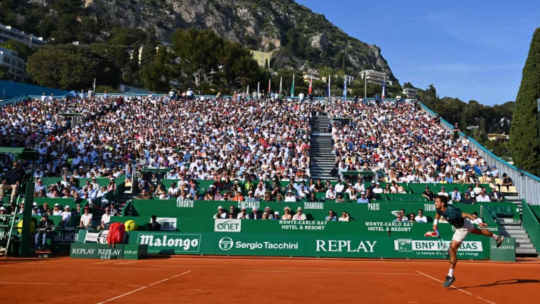 A player serving before a full stand in the evening sun at the Monte-Carlo Country Club, the Rolex Monte-Carlo Masters, Monte Carlo, an April engagement in the season calendar of The Mansa Court