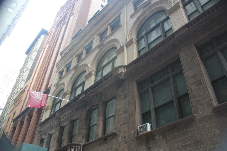 The arched brick and brownstone façade of the Down Town Association on a grey winter day, a red banner hung from the façade (2021).